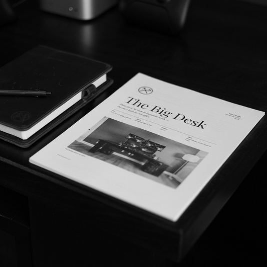 Printed cover of The Big Desk plans, showing a photo of the finished desk, on a dark desktop next to a leather notebook and pen